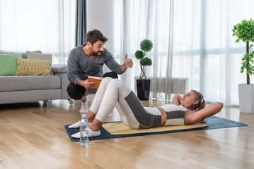Foto op Canvas Young business woman hiring private personal fitness trainer or coach to train her in her apartment. Woman with health issue after car crash accident exercising at her home with friend helping her. © Srdjan
