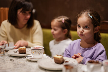 Mother with daughters eating desserts together at cozy cafe and having fun.