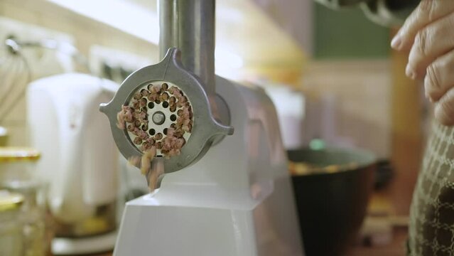Woman making minced meat for patte with an electric meat grinder in the kitchen