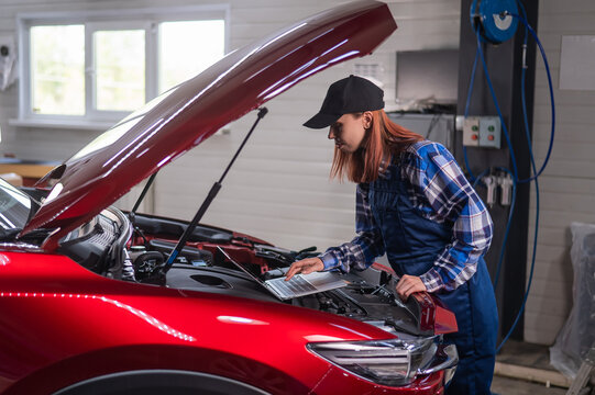 Woman auto mechanic doing engine diagnostics using laptop. 