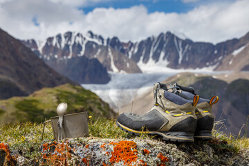 Trekking boots, titanium mug and spoon on the background of the Alpine valleys. Objects in focus,...