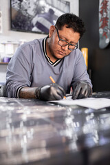 A tattoo artist is drawing a design stencil on his work stretcher before tattooing