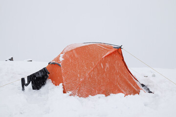 Orange tent in the mountains covered with snow.