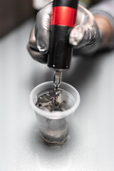 Close up of a tattoo artist is pouring ink into a plastic glass to clean the needle