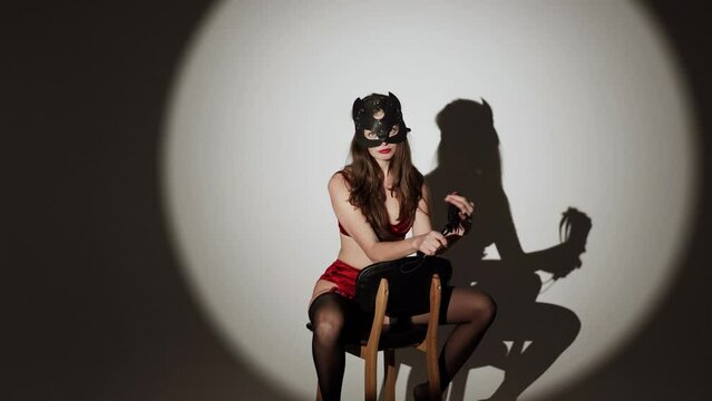 Sexy woman with long hair in red lingerie and stockings posing with bdsm cat mask and whip in studio.Сoncept of role-playing games and bdsm