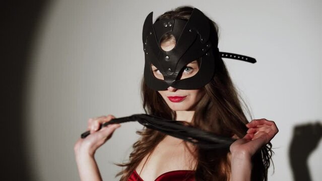 Sexy woman with long hair in red lingerie and stockings posing with bdsm cat mask and whip in studio.Сoncept of role-playing games and bdsm