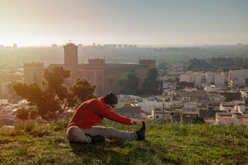 Man sitting doing stretching on top of a hill with landscape of a European medieval village at sunrise