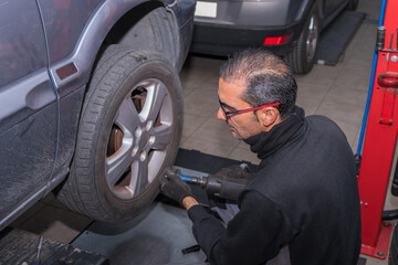 The mechanic uses a tool to remove the nuts from the wheels of a car.