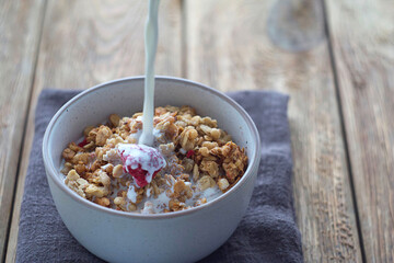 A plate of muesli stands on a wooden table. Someone pours cream into muesli. selective focus
