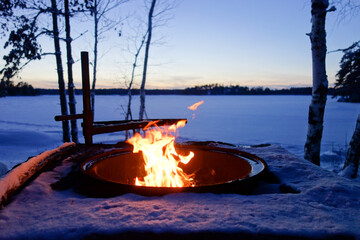 Campfire in the evening by snowy frozen lake in the wilderness in Finland 