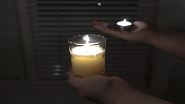 Two burning candles in the hands against the background of a window with blinds