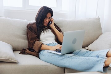 Woman blogger with phone lying at home and talking on the phone on sofa with laptop and working freelancer online, selfie