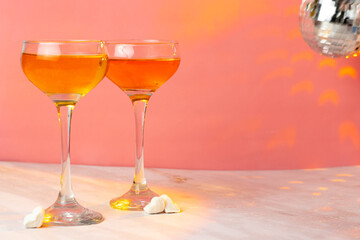 Orange cocktail with tall glasses on a pink background. Two glasses