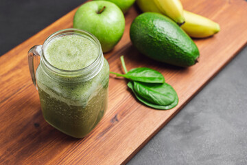 Green smoothie drink blended in a glass jar, avocado, spinach leaves, banana and apples at wooden...