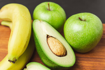 Sliced halves of avocado, banana and apple fruits on a wooden board, ingredients for cooking