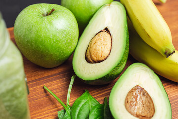 Sliced halves of avocado, banana and apple fruits on a wooden board, ingredients for cooking