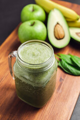 Green smoothie drink blended in a glass jar, avocado, spinach leaves, banana and apples at wooden board