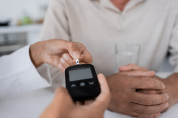 partial view of african american doctor showing test strip on glucometer device to middle aged patient