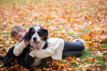 Outdoor portrait of boy hugging bernese mountain dog in autumn. Friendship of teenager with pet.