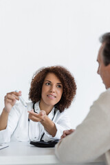 cheerful african american doctor pointing with finger at lancet pen near middle aged patient with diabetes in clinic