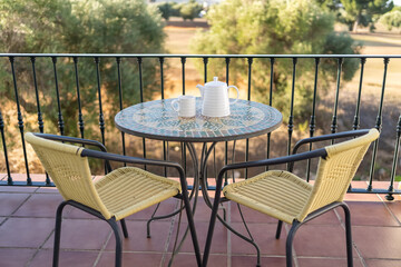 Apartment terrace with table and two chairs and views of the outside garden on a sunny day.
