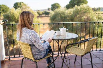 Woman reading a book sitting on a terrace overlooking the outside on a peaceful and relaxed day.