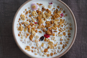 A plate of muesli with raspberries and raisins stands on a wooden table. There is a towel under the plate.  Top view