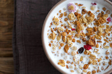 A plate of muesli with raspberries and raisins stands on a wooden table. There is a towel under the plate. Top view