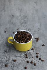 Roasted coffee seeds on yellow mug isolated on gray background