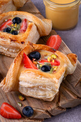 Puff pastry buns with custard, strawberry and blueberry served on wooden board