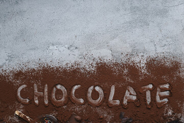 Chocolate stuff. Word chocolate written on cocoa powder with processed chocolate food, biscuit, chocolate bar, cookies and muffin isolated on gray background. 
