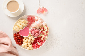 Fototapeta na wymiar Romantic coffee for two, heart shaped lollypop and Valentine's Day charcuterie board with chocolate sweets and strawberries on white background. Copy space.
