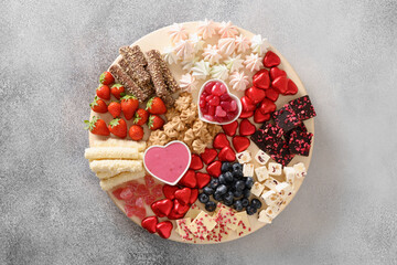 Charcuterie Valentines Day board with chocolate, red hearts, different sweets, strawberries, blueberries and candies on gray background. View from above.