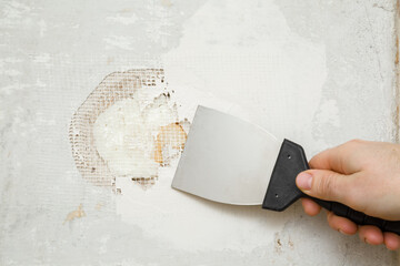 Young adult man hand using spatula and plastering concrete wall hole with putty on mesh. Closeup. Repair work of home. Renovation process. - obrazy, fototapety, plakaty