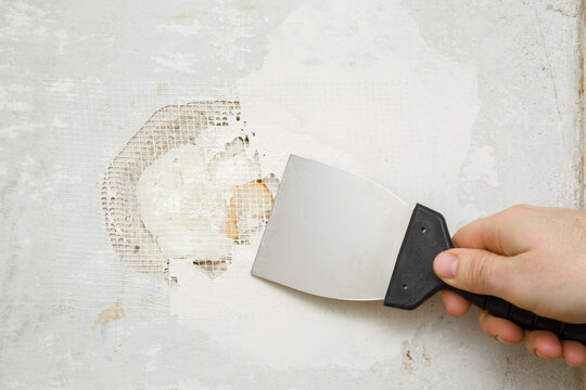Young adult man hand using spatula and plastering concrete wall hole with putty on mesh. Closeup. Repair work of home. Renovation process.