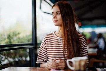 A beautiful woman with red hair sits in a cafe with a mug of coffee and smiles, freelance lifestyle