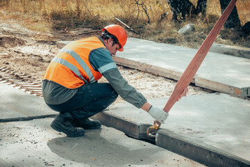 Slinger lays concrete slab on construction site on summer day. Worker in protective vest and...