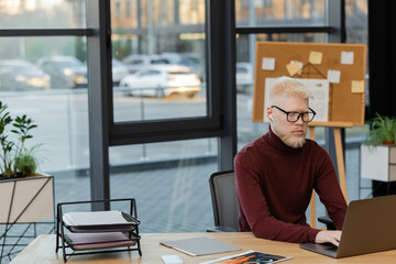 bearded albino businessman in wireless earphone using laptop while working in office