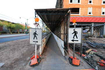 Pedestrian signs by entrance of walkway tunnel with barricades and scaffolding at construction site