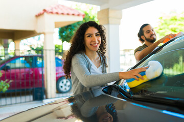 Latin couple looking happy while doing car wash chores