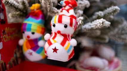 Tiny figurine snowman in colorful outfit in front of snowy pine tree, blurred background, with space and text space