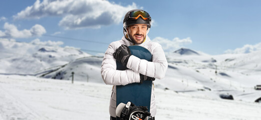 Young man hugging a snowboard and posing on a mountain