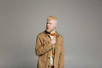 bearded albino man in stylish shirt jacket and silk scarf posing isolated on grey
