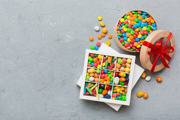 Set of different sweet candy in a paper box with a satin ribbon on a colored background. Holiday concept