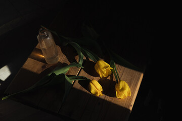 From above of yellow tulips placed on wooden table with glass vase in sunlit room 