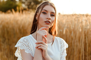 Tranquil beautiful woman in white dress with long hair looking at camera against wheat field in...