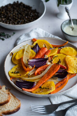 Plate with oven baked vegetables (pumpkin, carrot, pepper, onion) and bowl with lentil on white surface.