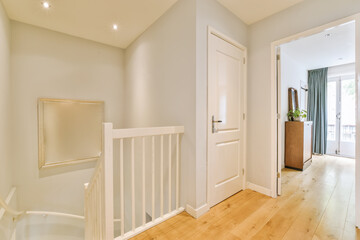 a room with white walls and wood flooring on the side of the stairs, there is an open door leading...