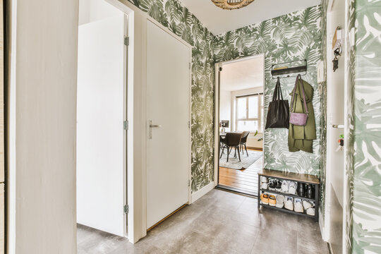 a hallway with green and white wallpaper on the walls, an entry way leading to another room is in the background