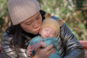 Obraz premium outdoors lifestyle portrait of young happy and beautiful Asian Chinese woman as mother of little adorable baby girl holding her tender and sweet in city park on sunny day